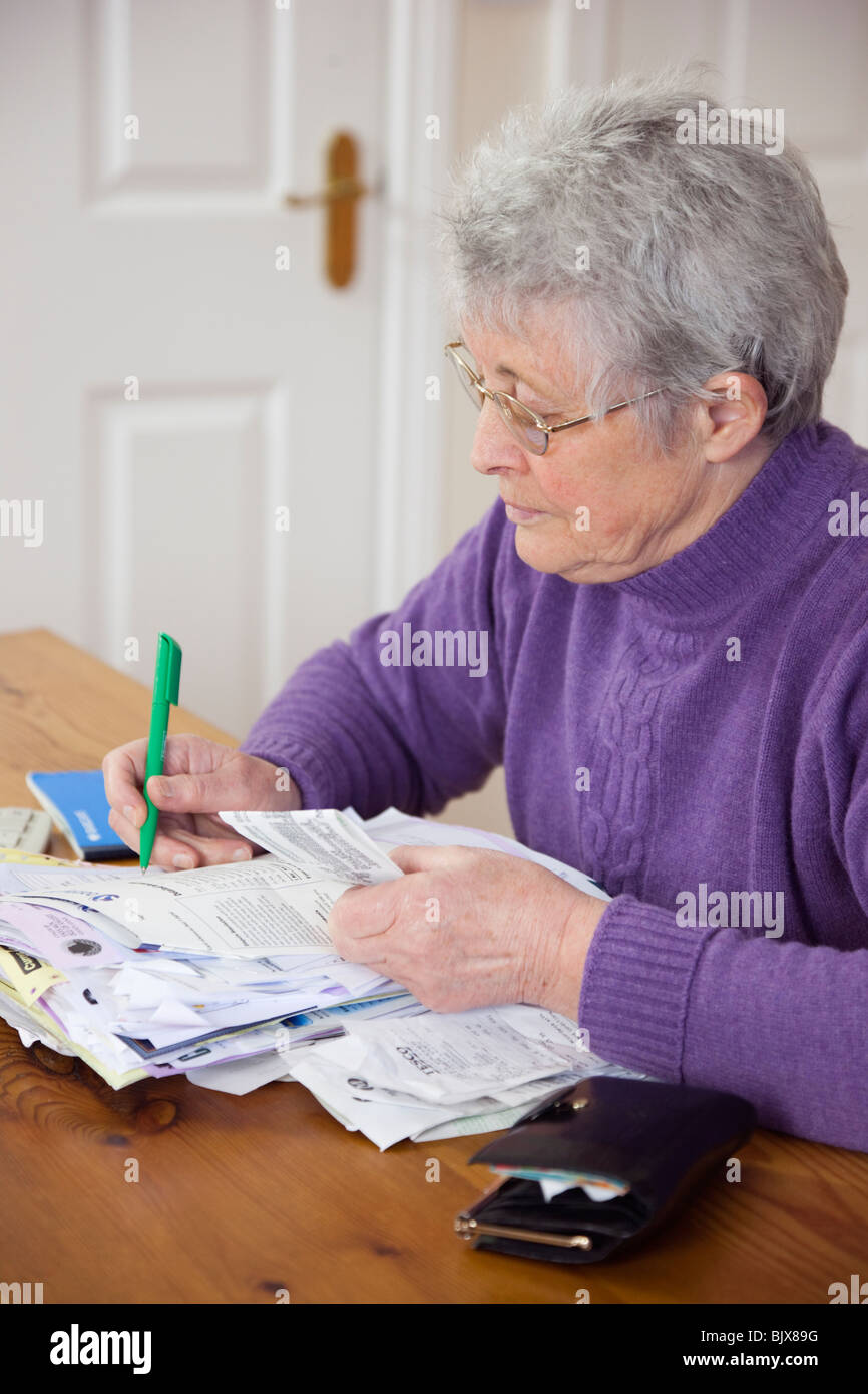 Ältere Frau Rentner OAP Dame zu Hause mit einer Vielzahl von Rechnungen auf dem Tisch die Kontrolle einer Kreditkarte Aussage gegen die Quittung. Großbritannien Großbritannien Stockfoto