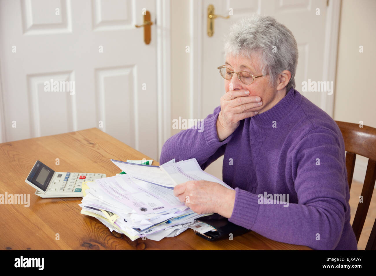 Ältere Frau Rentner mit einem großen Stapel von Rechnungen auf eine Tabelle mit der Hand über den Mund in großer Rat Steuern in Zeiten der Sparpolitik UK schockiert Stockfoto