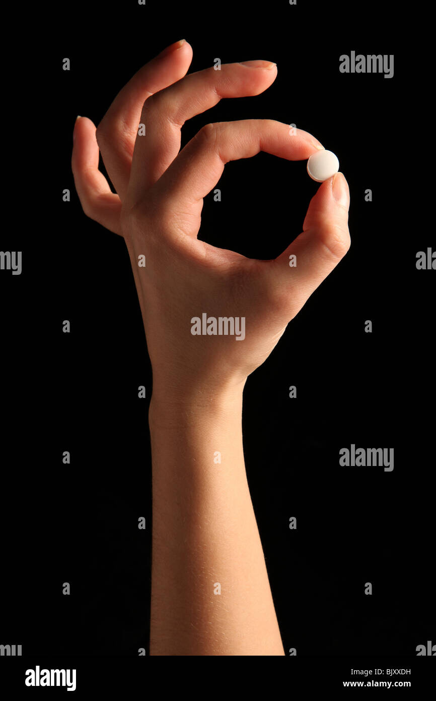 Eine weibliche Hand eine kleine weiße Pille zwischen den Fingern Stockfoto