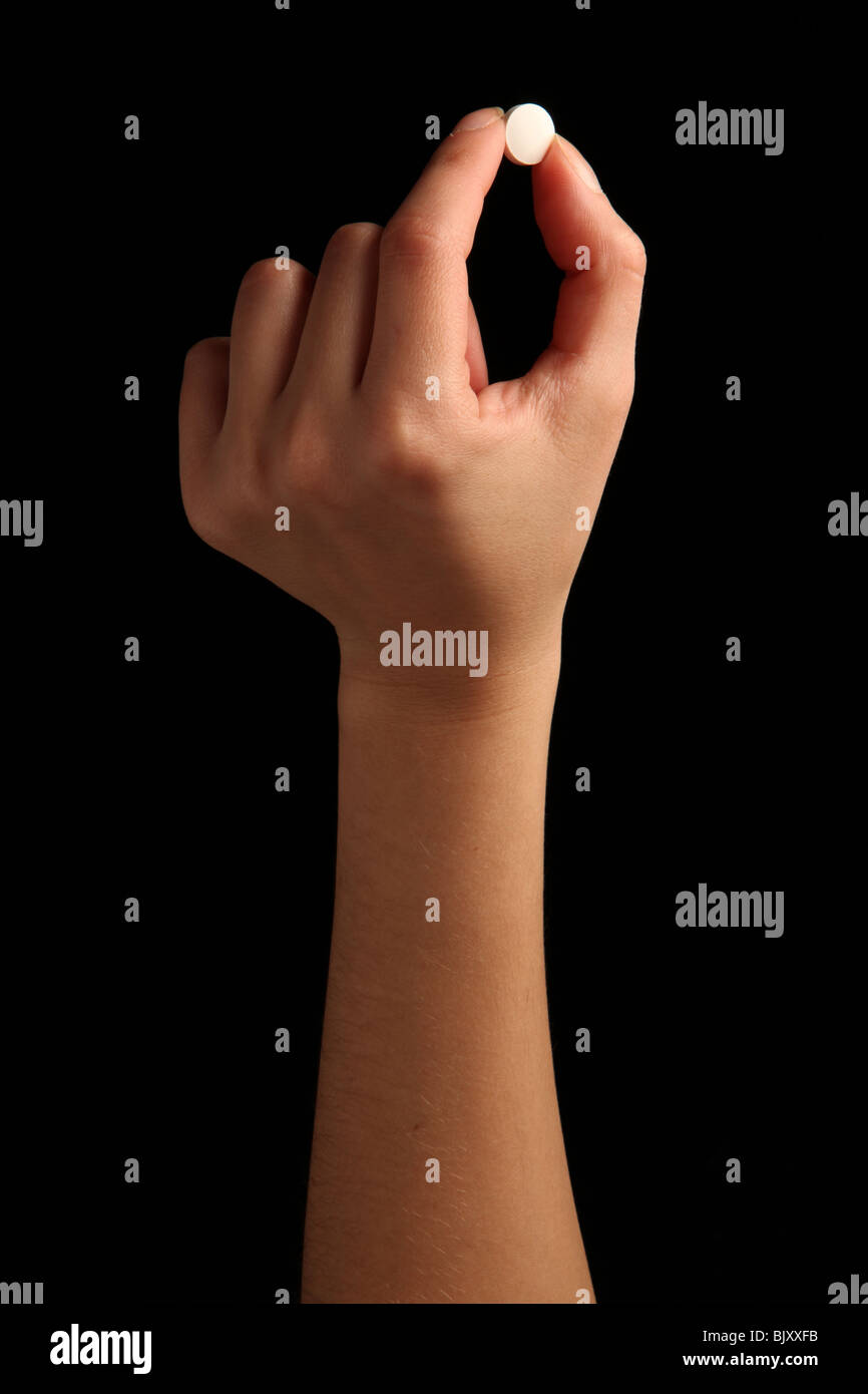 Eine weibliche Hand eine kleine weiße Pille zwischen den Fingern Stockfoto