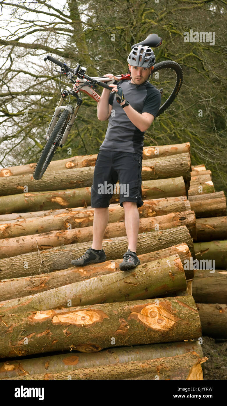 junger Mann mit seinem Mountainbike über einen großen Stapel von geschnittenen Protokolle Stockfoto