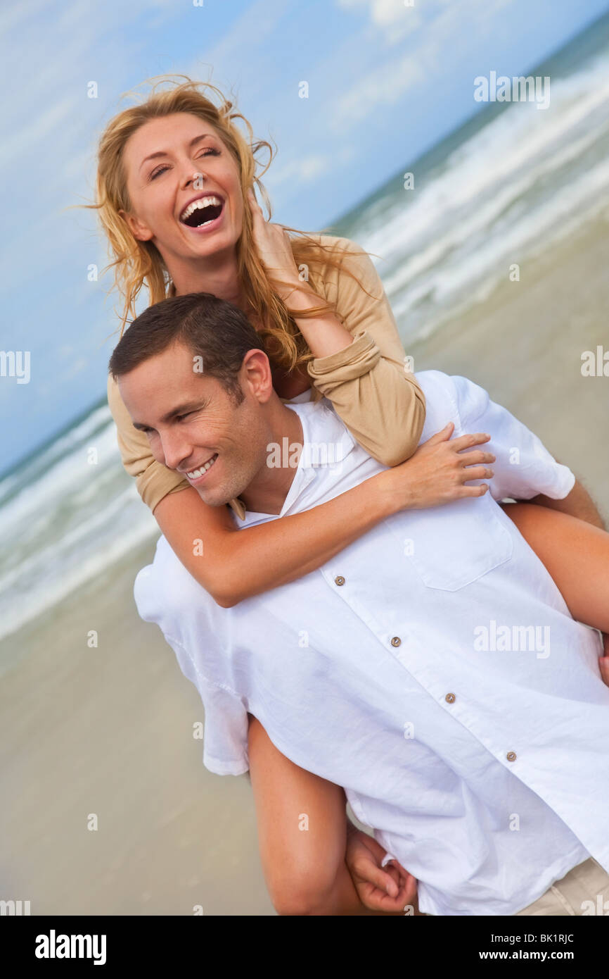 Ein junger Mann und Frau Spaß als romantisch zu zweit an einem Strand mit der Mann die Frau auf seinem zurück Piggy back Stil. Stockfoto