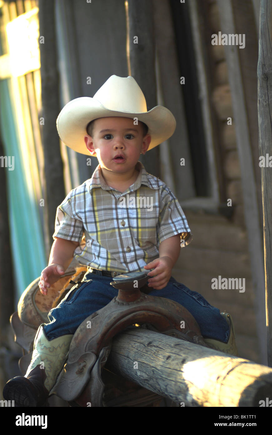 Ein niedlich 2-4 jährige Mischlinge junge sitzen auf einem Sattel und tragen eine Cowboy-hat(Released) Stockfoto