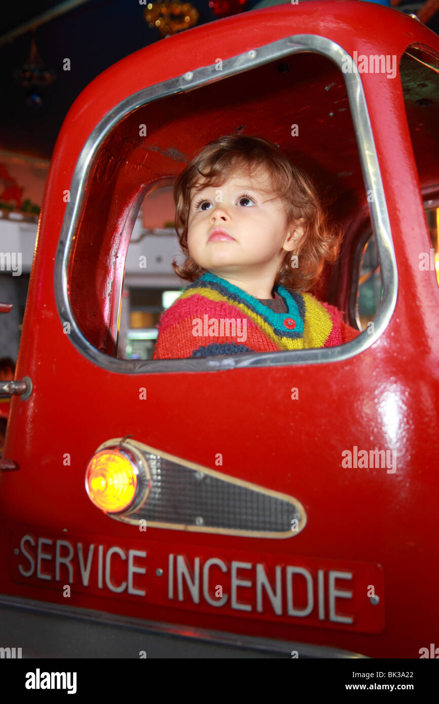 22 Monate altes Mädchen im Inneren ein Feuer-Auto-Karussell in Bewegung Stockfoto