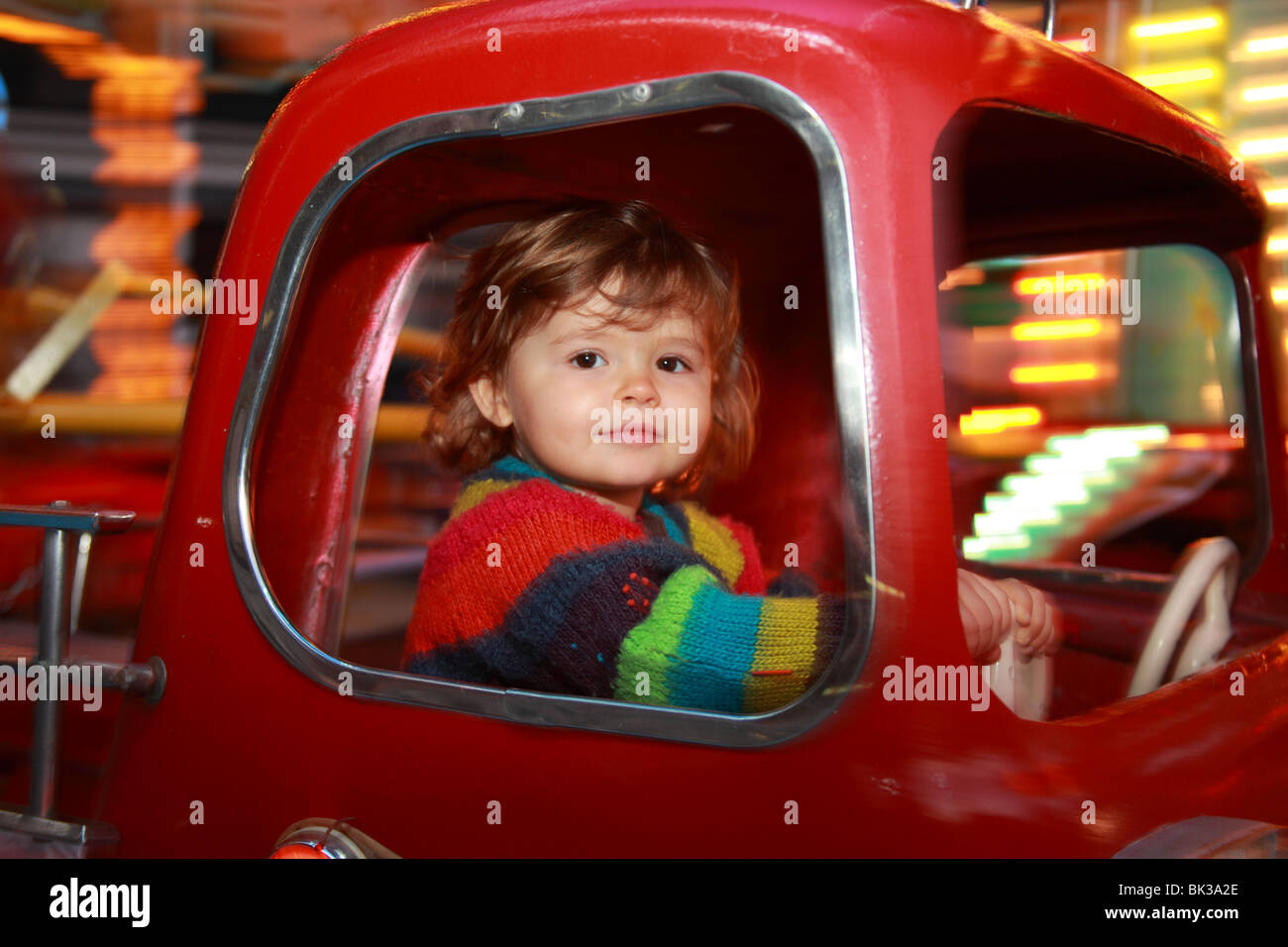 22 Monate altes Mädchen im Inneren ein Feuer-Auto-Karussell in Bewegung Stockfoto