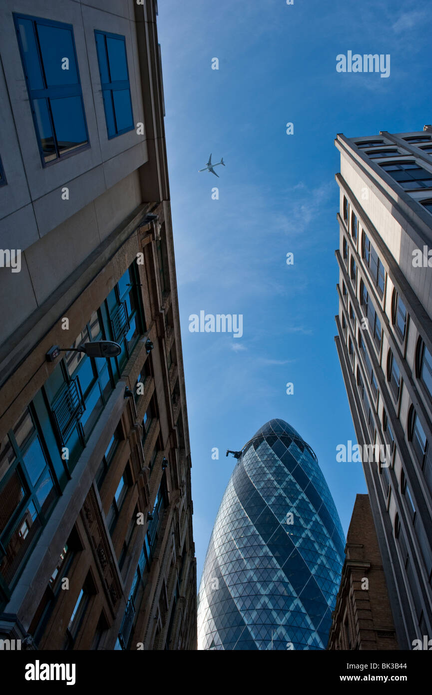 Blick auf die 30 St Mary Axe von der Unterseite mit einem Flugzeug am Himmel überqueren. Stockfoto