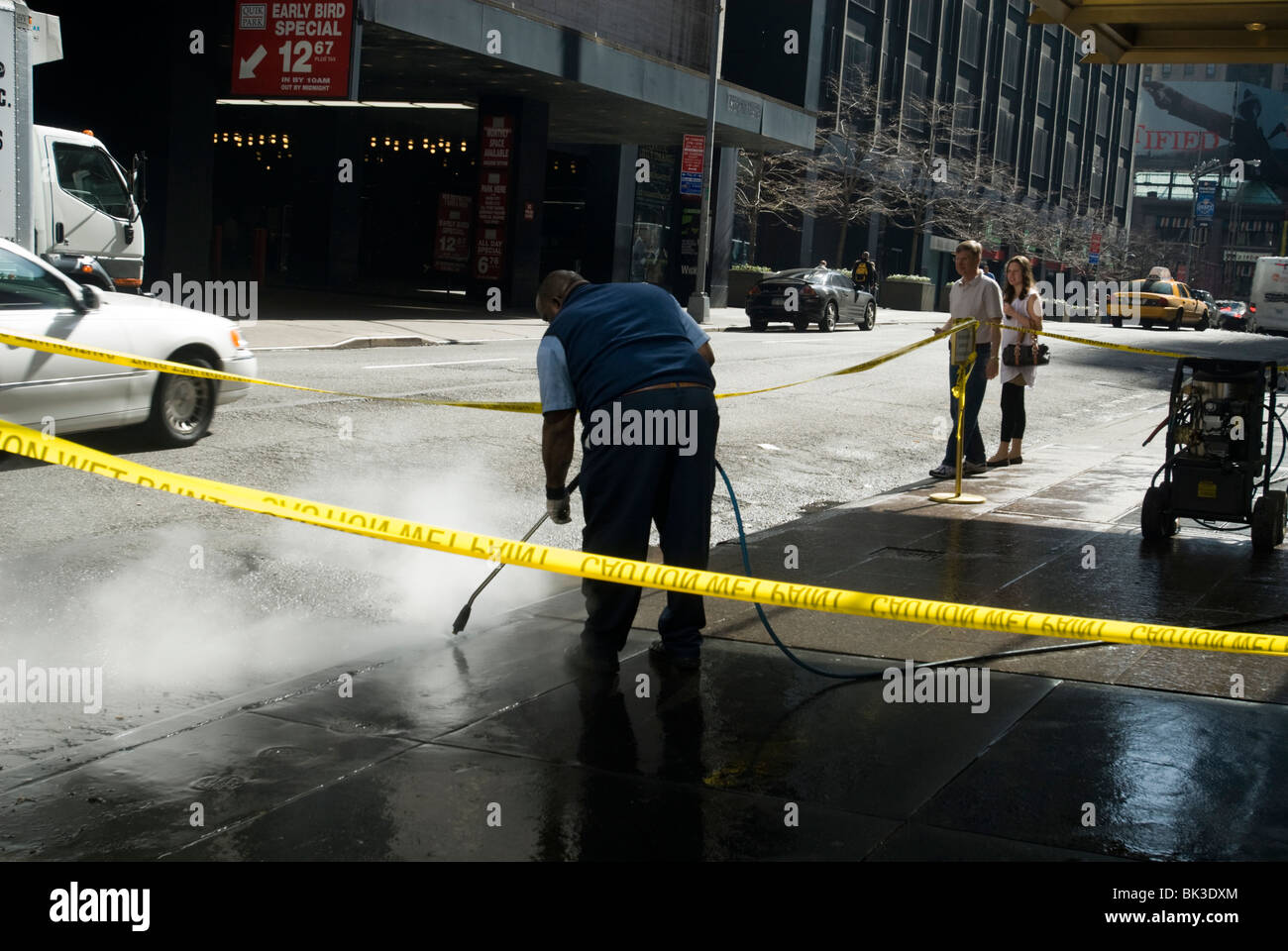 Ein Arbeitnehmer nutzt ein Hochdruck-Wasserschlauch auf einen Bürgersteig in New York zu reinigen Stockfoto