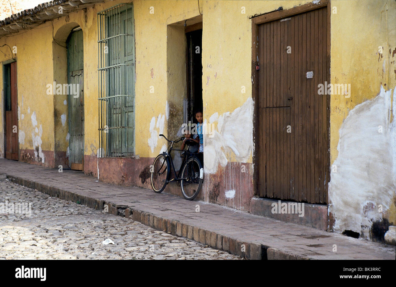 Straßenszene mit einem Fahrrad und zwei Kindern in einer Tür der kolonialen Struktur, die in der Stadt Trinidad, Kuba, in Verfall ist Stockfoto