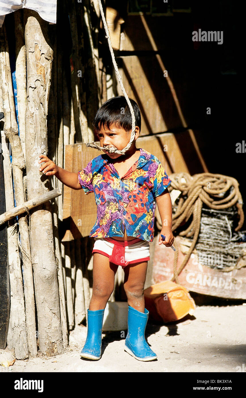 Porträt eines jungen Kindes, das in Guatemala, Mittelamerika, an einem Seil kaut und blaue Gummistiefel trägt Stockfoto