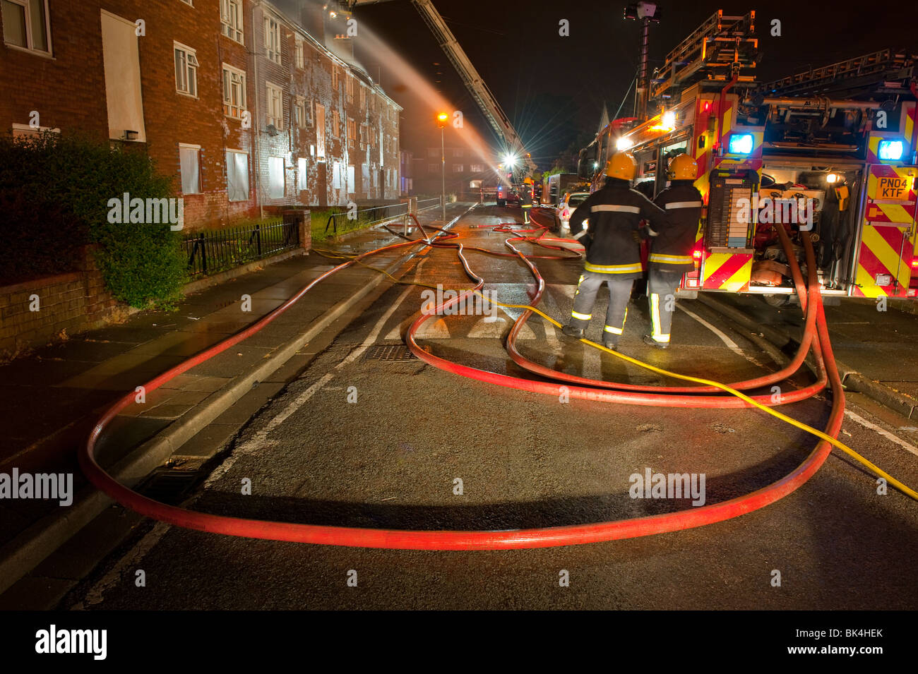 Hausbrand mit Feuerwehrauto und Schlauch in der Nacht Stockfoto