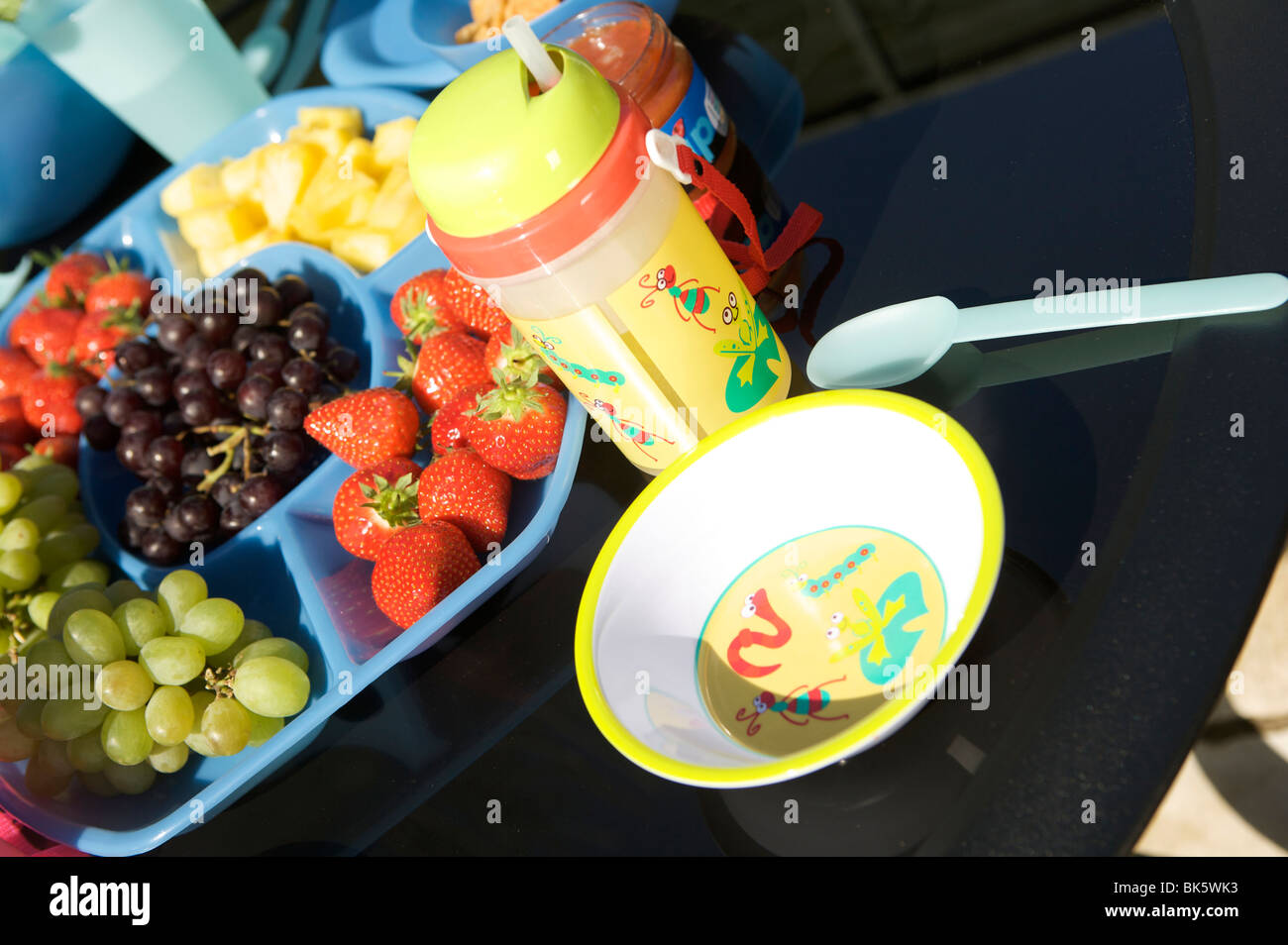 Im Freien essen oder ein Picknick auf einem schwarzen Tisch mit blauen Kunststoff Schüsseln, Tassen und Krüge mit Obst und Salat Stockfoto