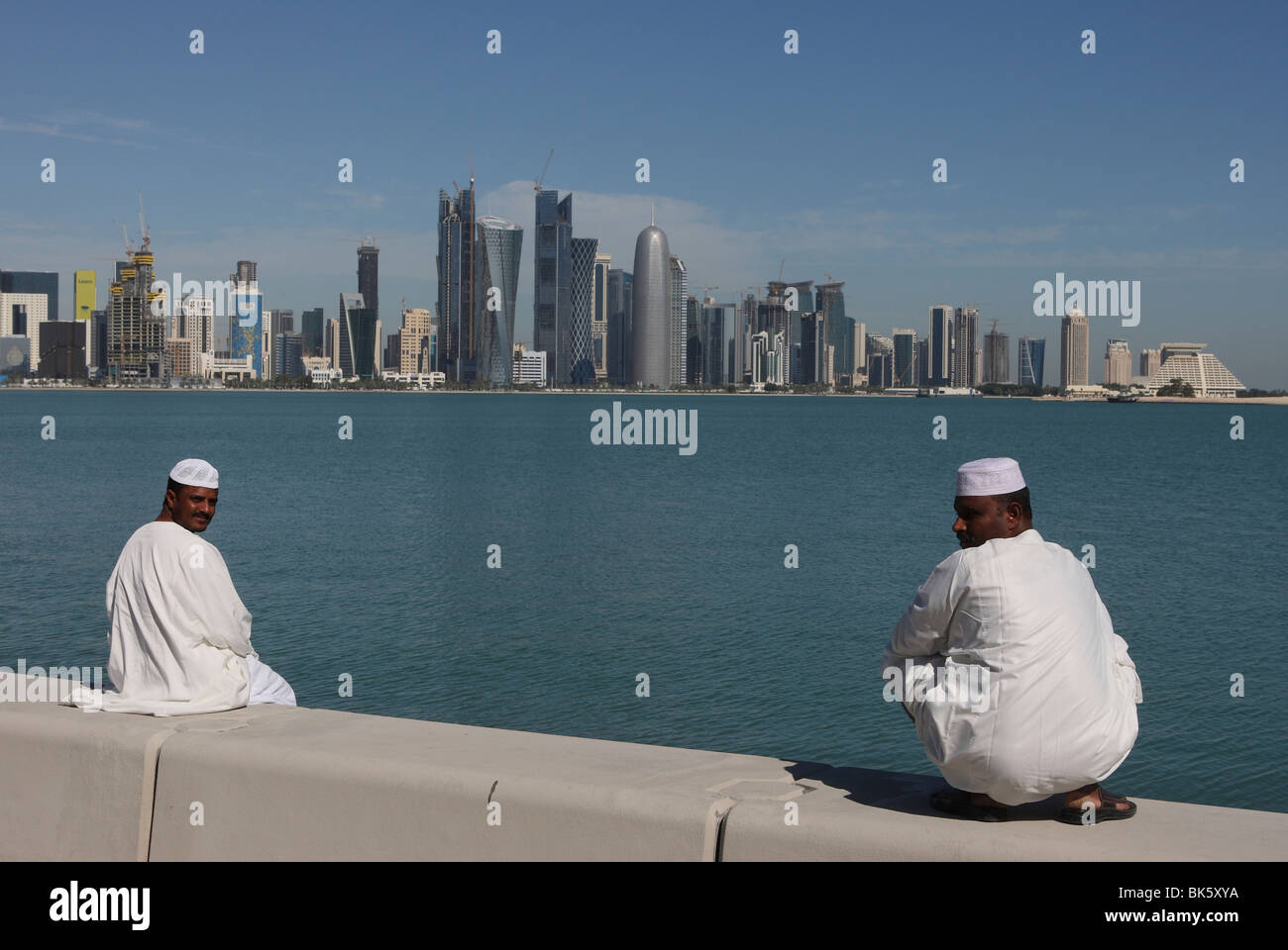 Zwei arabische Männer sitzen auf Wand mit West Bay Skyline von Doha im Hintergrund. Stockfoto