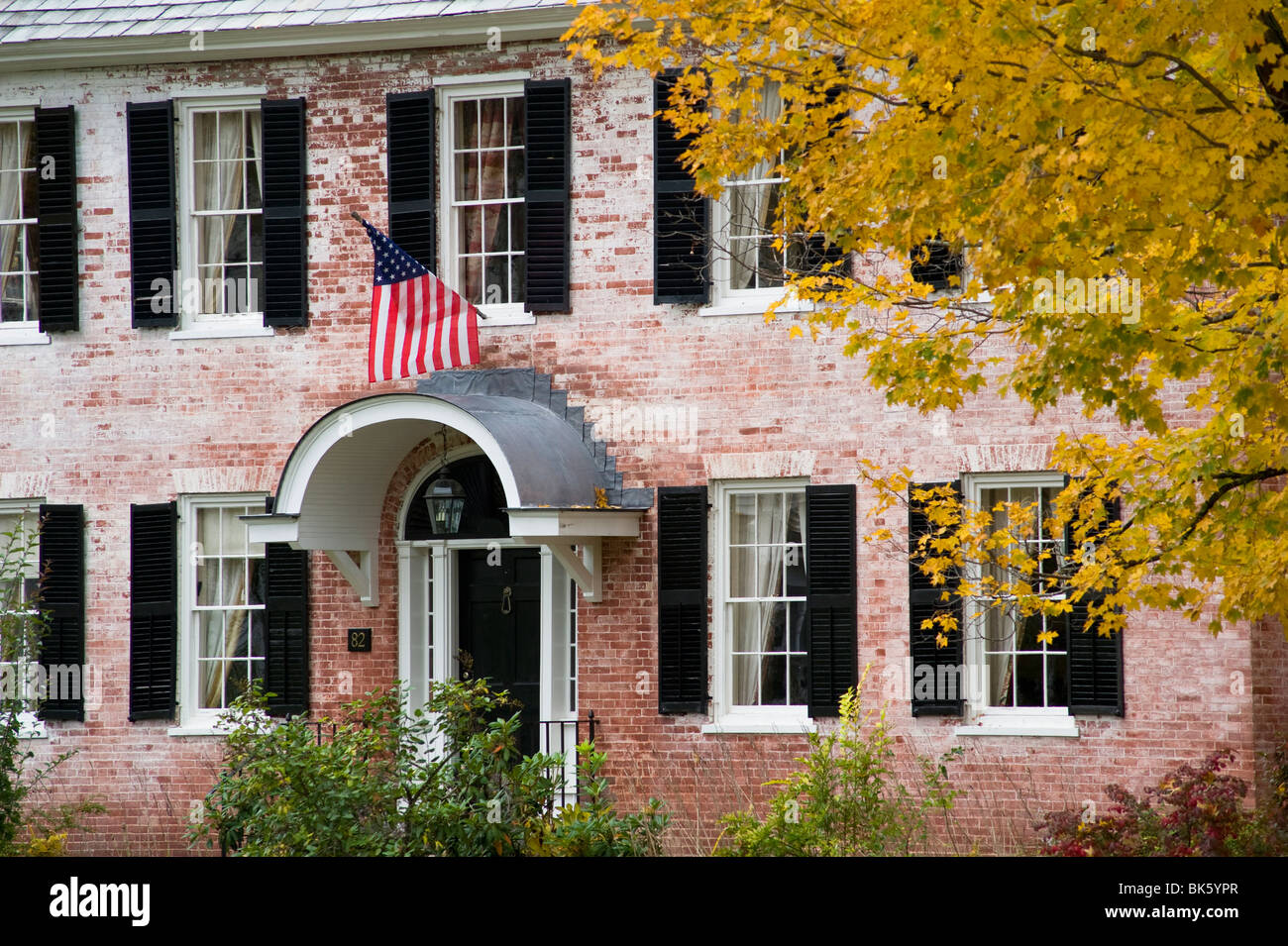 Ein altes Backsteinhaus zeigt eine amerikanische Flagge und umgeben von Herbstlaub in Townshend, Vermont, USA Stockfoto