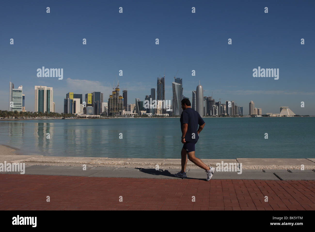 Mann Joggen entlang der Corniche mit West Bay Skyline von Doha im Hintergrund. Stockfoto