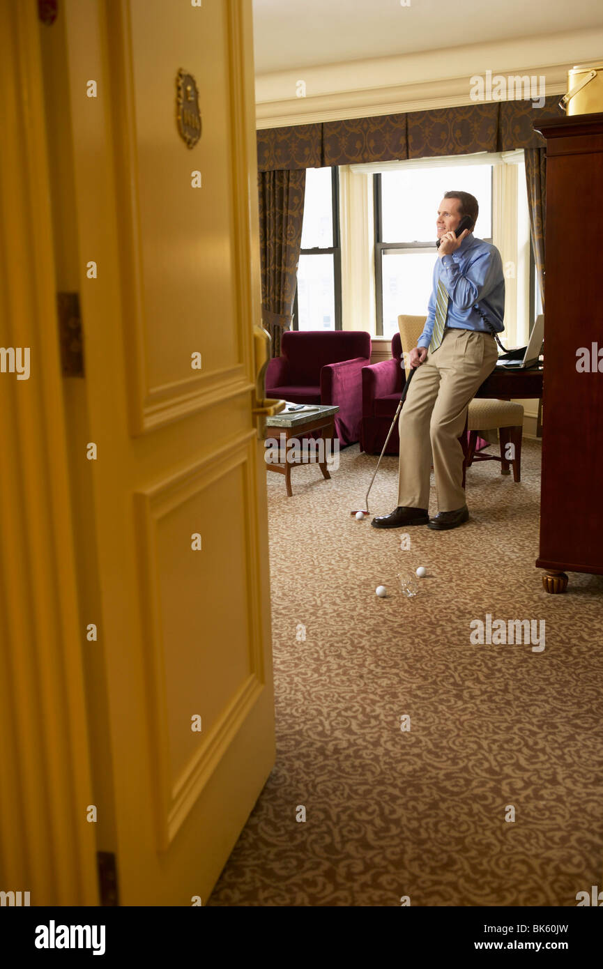 Geschäftsmann am Telefon zu sprechen, während putting Golfbälle in seinem Hotelzimmer Stockfoto
