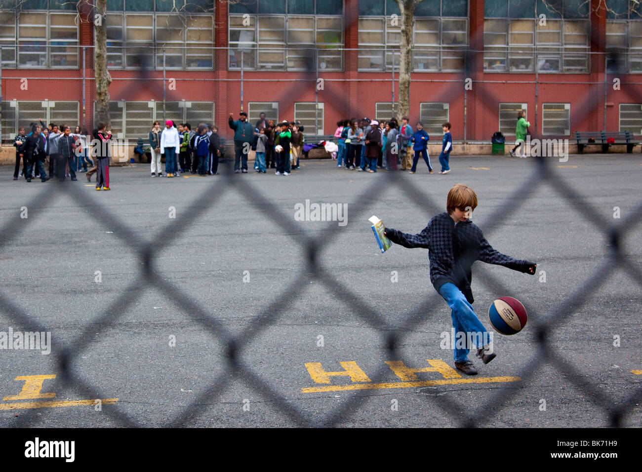 Junge treten Ball, hält Buch auf einem Schulhof, Manhattan, New York City Stockfoto
