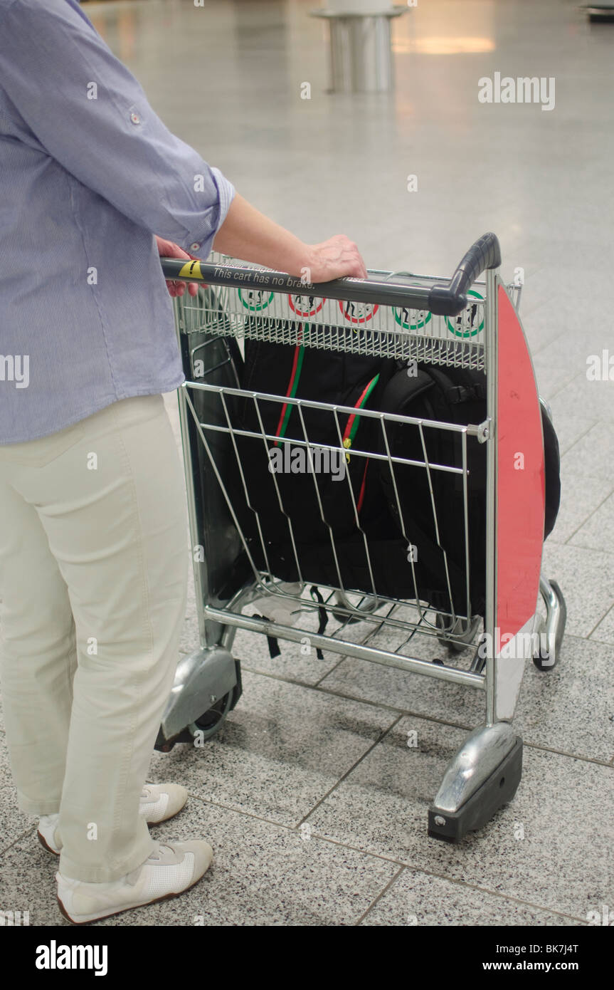 Frau am Flughafen mit Gepäckwagen. Warenkorb im Fokus Stockfoto