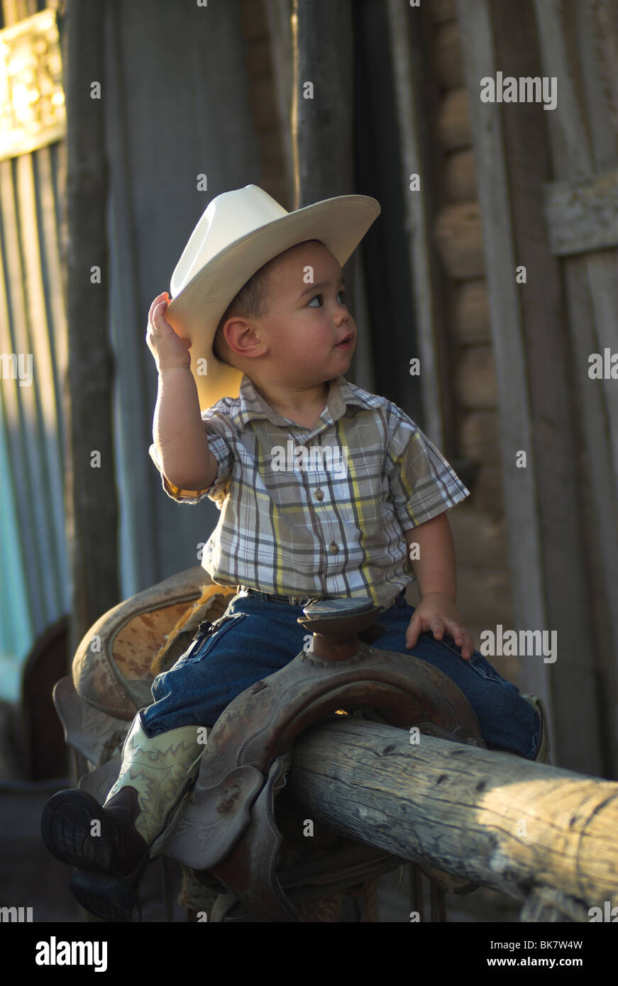 Ein niedlich 2-4 jährige Mischlinge Junge sitzt auf einem Sattel tragen eine Cowboy-hat(Released) Stockfoto