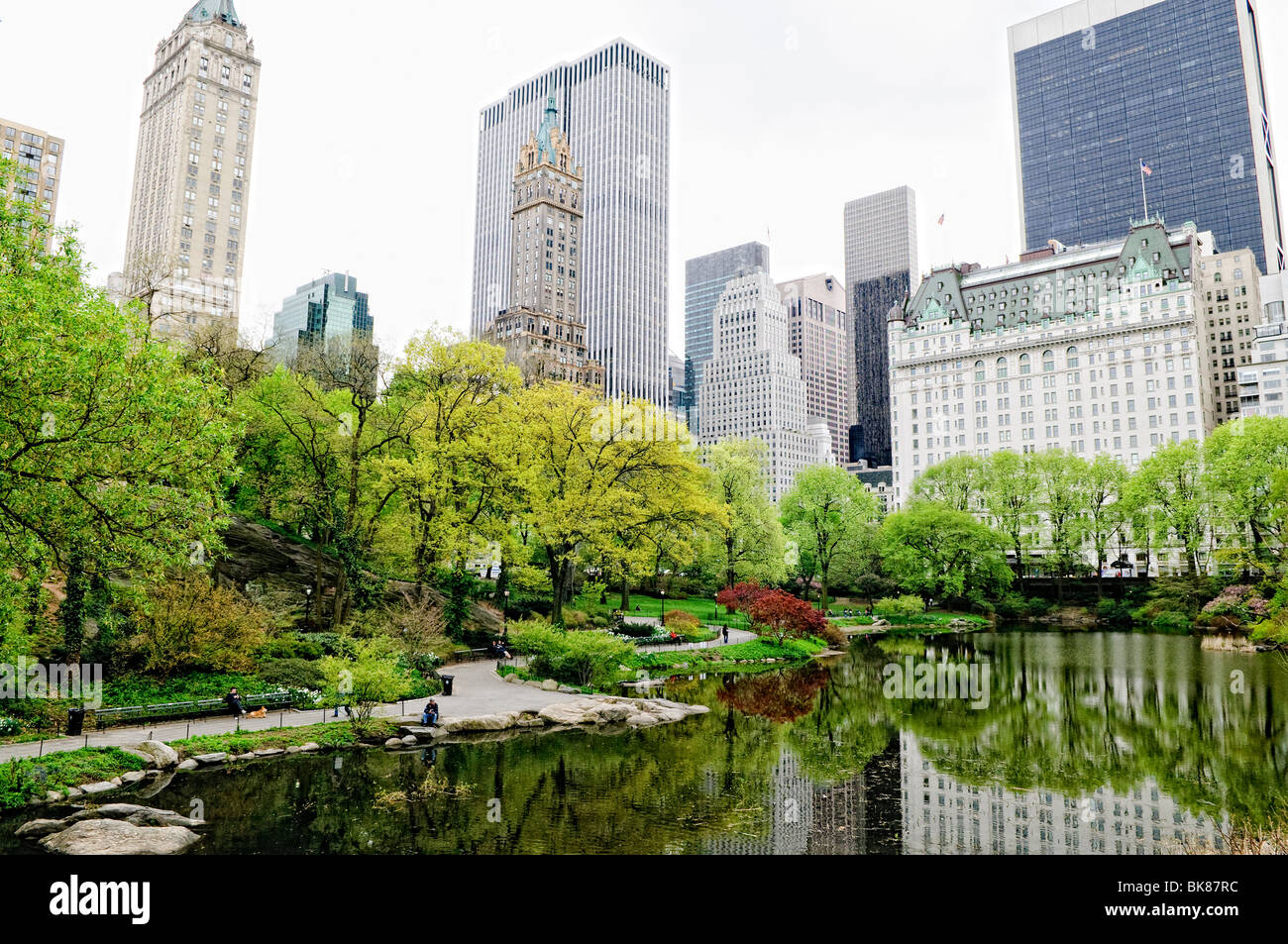Central Park The Pond Spring Laub New York City // NEW YORK, New York, Vereinigte Staaten – der Teich im New Yorker Central Park spiegelt die lebhaften Farben des Frühlings wider, mit blühenden Bäumen und frischem Laub rund um das ruhige Wasser. Im Hintergrund erhebt sich die berühmte Skyline von Manhattan über dem Park und schafft einen eindrucksvollen Kontrast zwischen der natürlichen Oase und der urbanen Landschaft von Midtown. Stockfoto