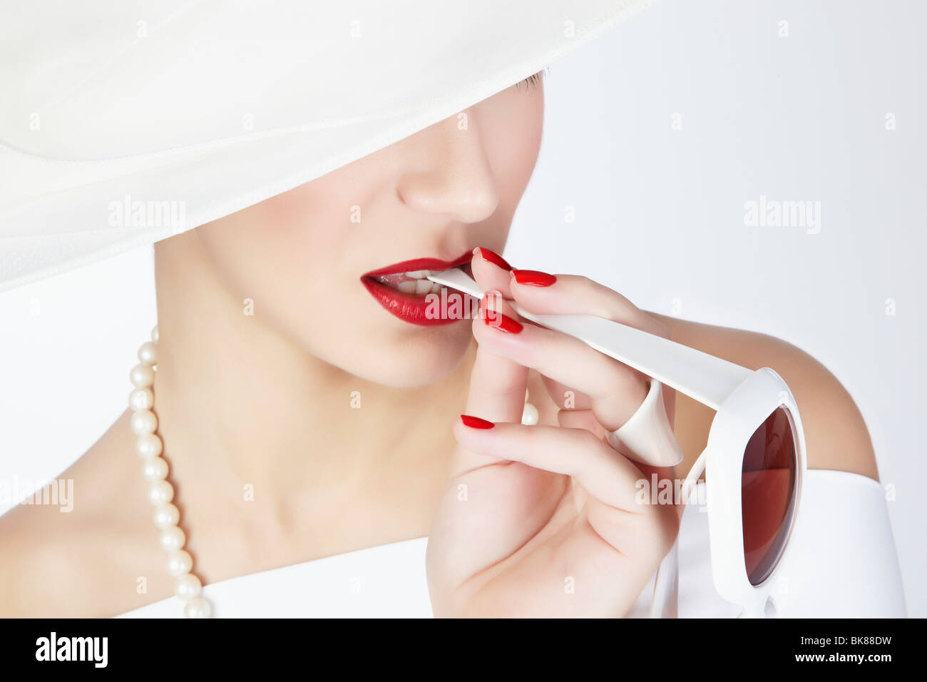 Porträt einer jungen Frau mit einem weißen Sommerhut, ein weißes Kleid und eine Perlenkette mit dem Arm ein paar weiße sunglasse Stockfoto