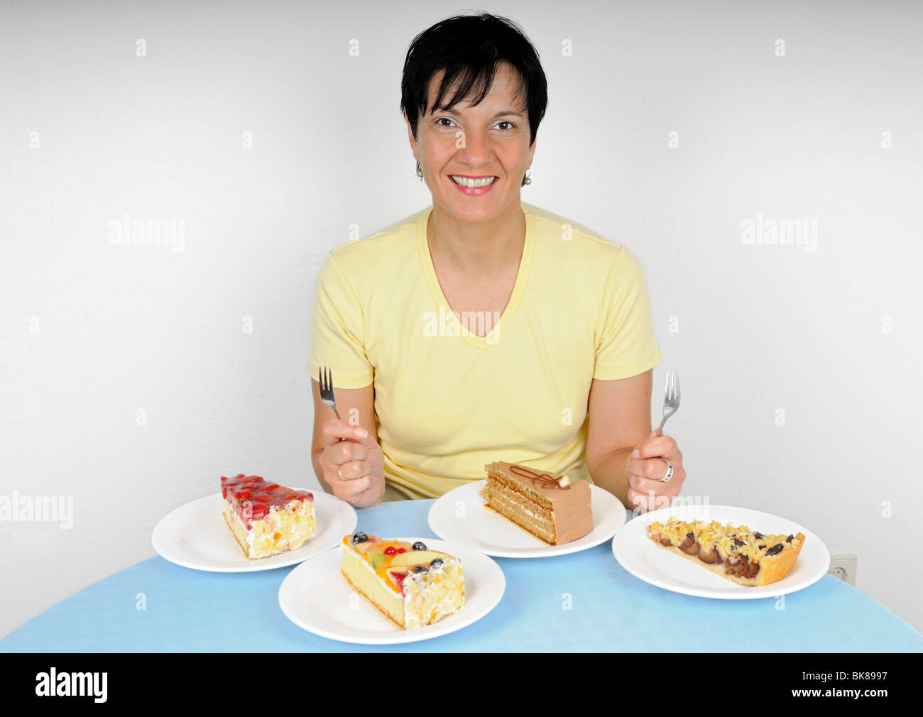 Frau sitzt gerne vor vier Platten mit Kuchen Stockfoto