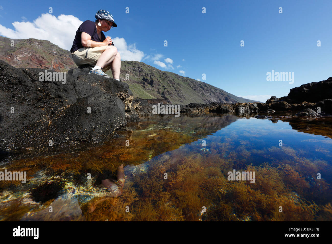 Frau sitzt auf einem Felsenpool einer felsigen Küste "Paisaje Protegido del Remo" Naturschutzgebiet, La Palma, Kanarische Inseln, Spanien Stockfoto