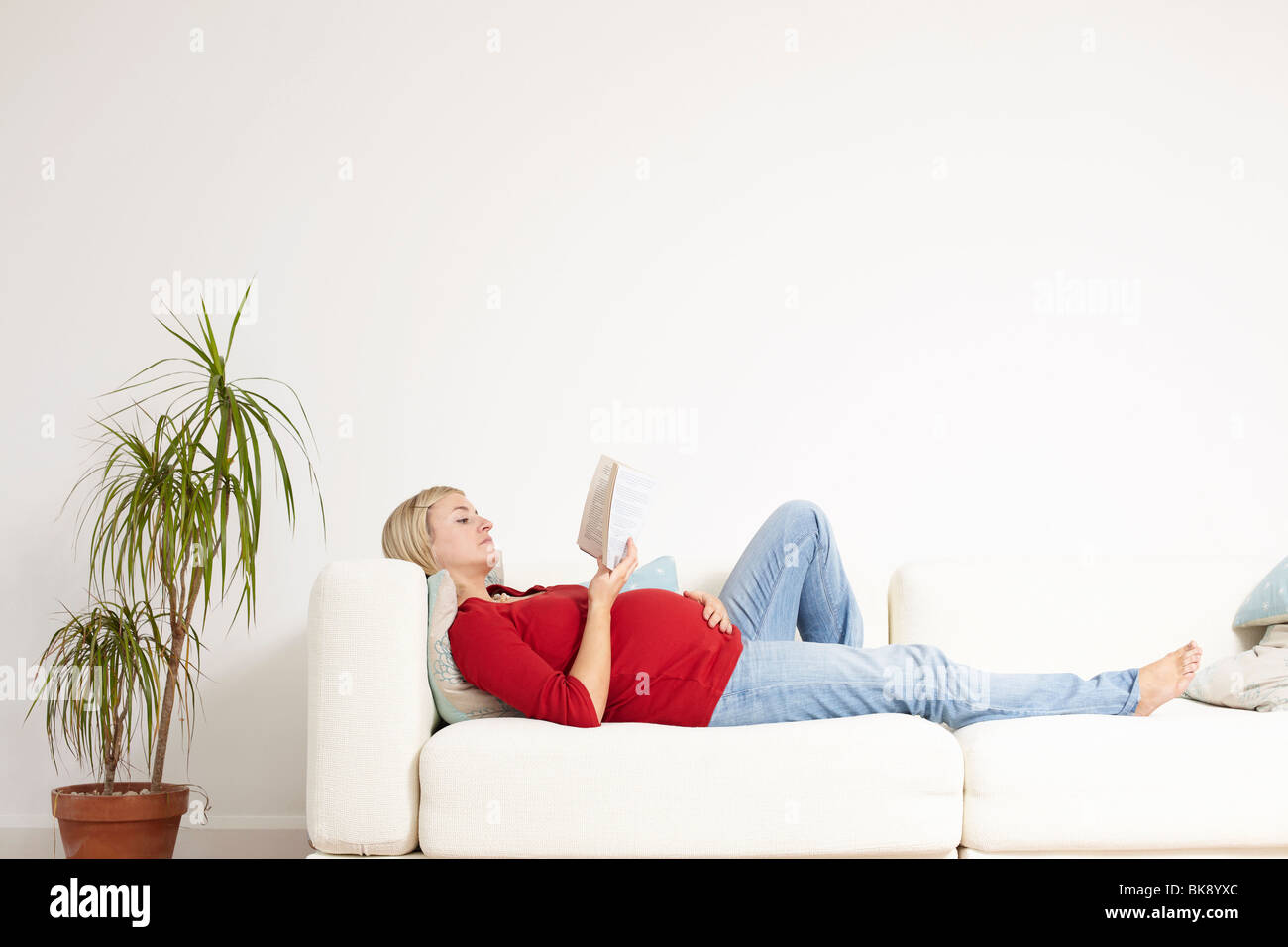 Schwangere Frau liest auf sofa Stockfoto