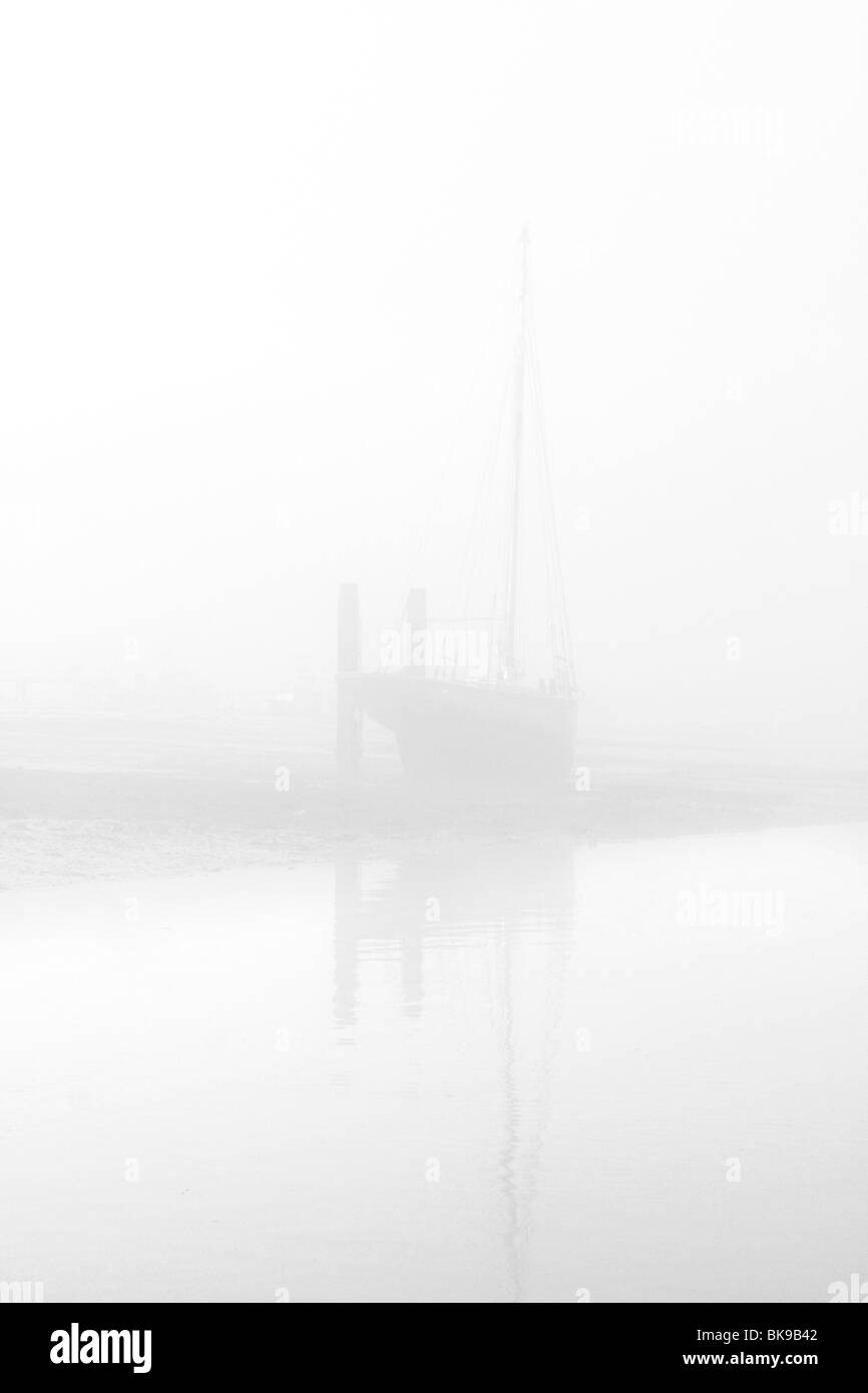 EIN VOR ANKER BOOT BEI EBBE IN DEN FRÜHEN MORGENNEBEL AM WEST MERSEA, ESSEX ABGEBILDET Stockfoto