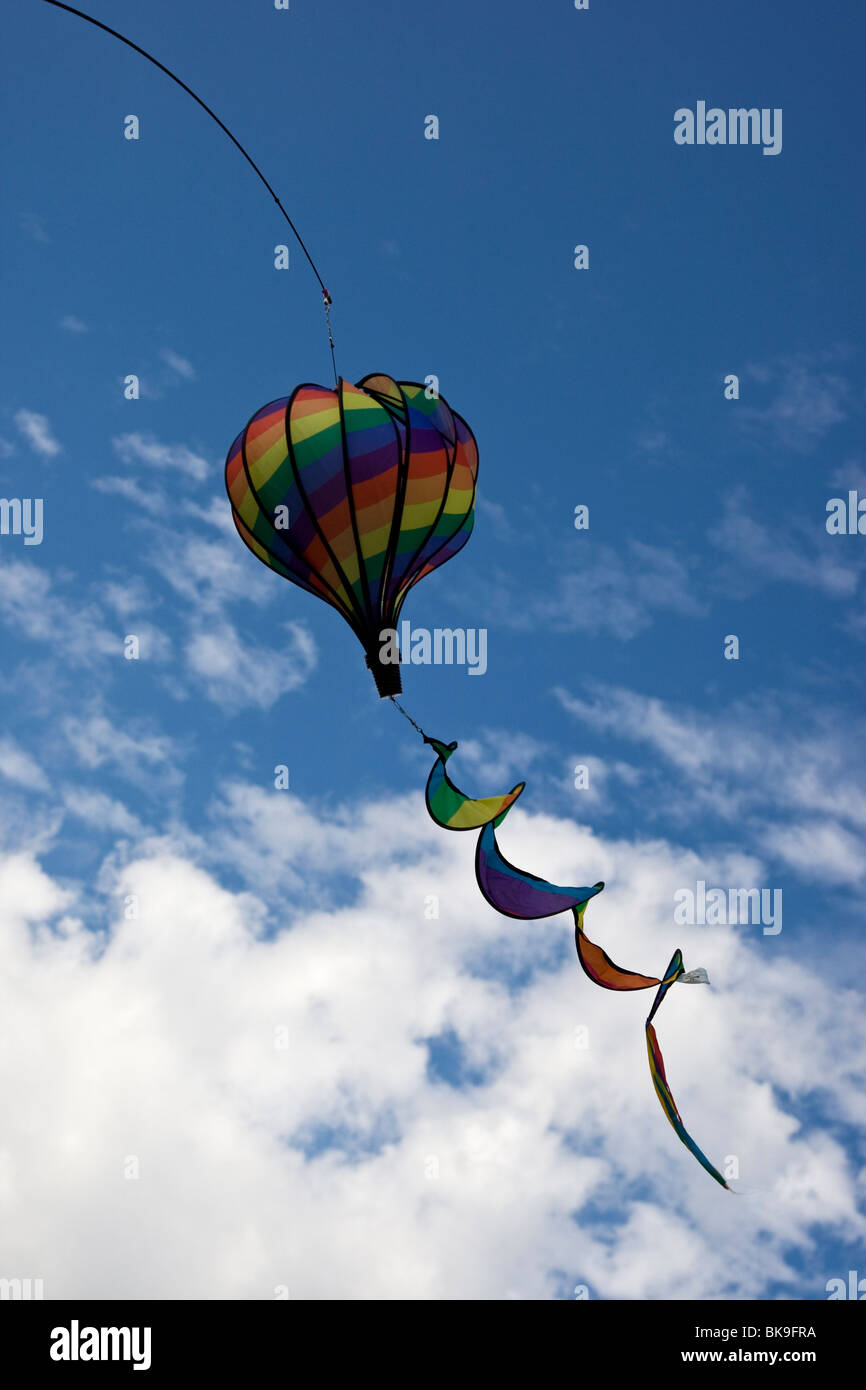 Bunte Drachen in Form von einem Heißluftballon fliegen in ein strahlend blauer Himmel mit dominanten flauschige weiße Wolken Stockfoto