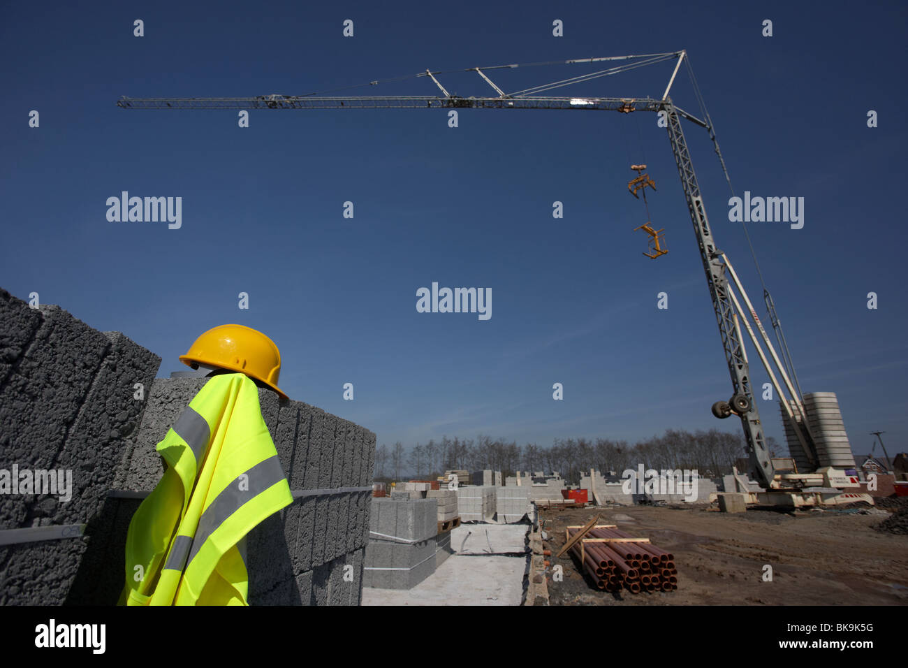 Schutzhelm und Hivis Weste auf einem Haufen von Brise Betonbausteinen mit selbstaufrichtendem Kran auf einer leeren Baustelle in großbritannien Stockfoto