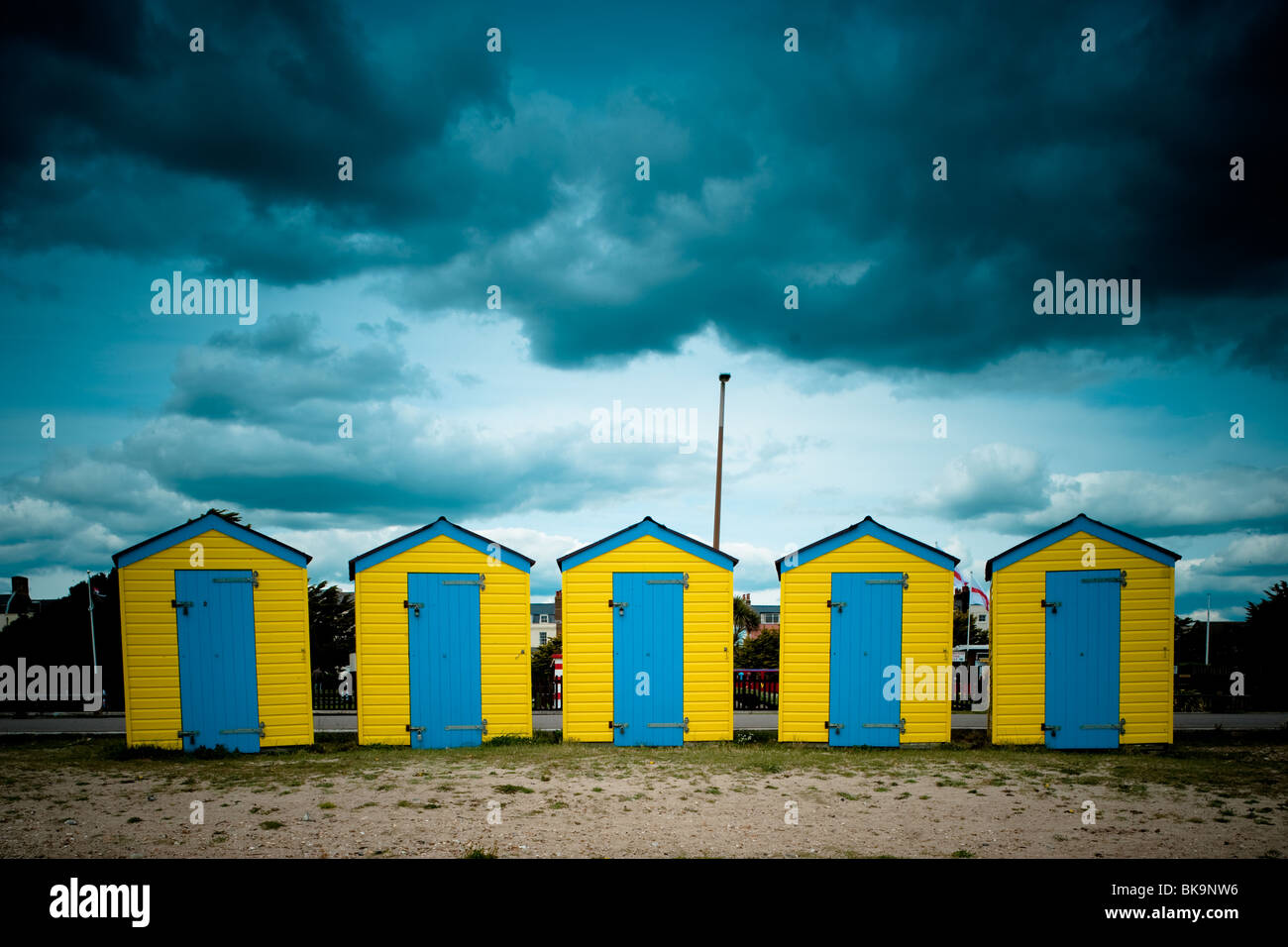 Gelb und blau Strandhütten unter ein stimmungsvoller Himmel am Strand von Littlehampton, West Sussex Stockfoto