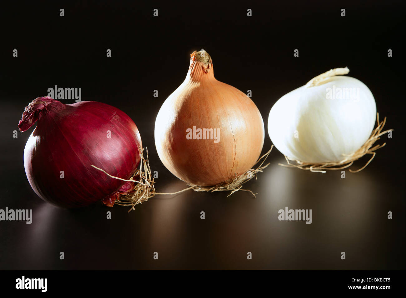 Drei bunte verschiedene Zwiebel in verschiedenen Farben auf schwarz Stockfoto