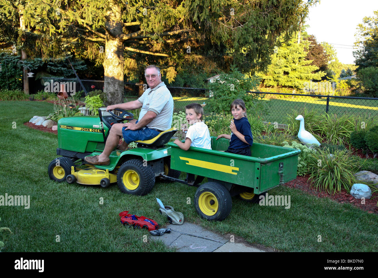 Großvater und zwei Enkelkinder sind mit Rasen Mover Trucktor außerhalb des Hauses mit Eis in der hand gezogen. Stockfoto