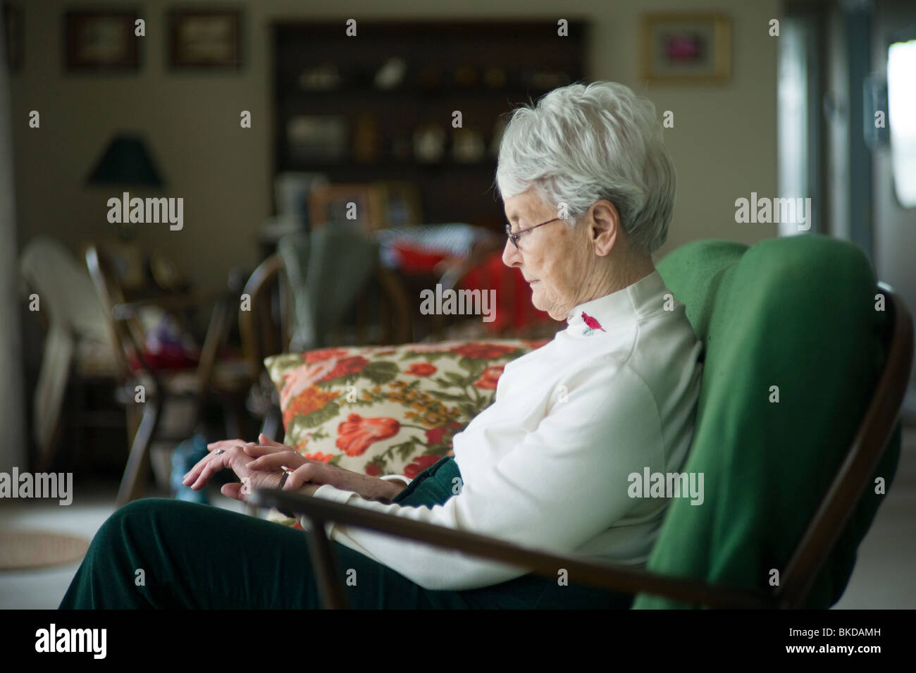 Alte Frau sitzt auf der Couch im Wohnzimmer starrte auf ihre Hände. Stockfoto