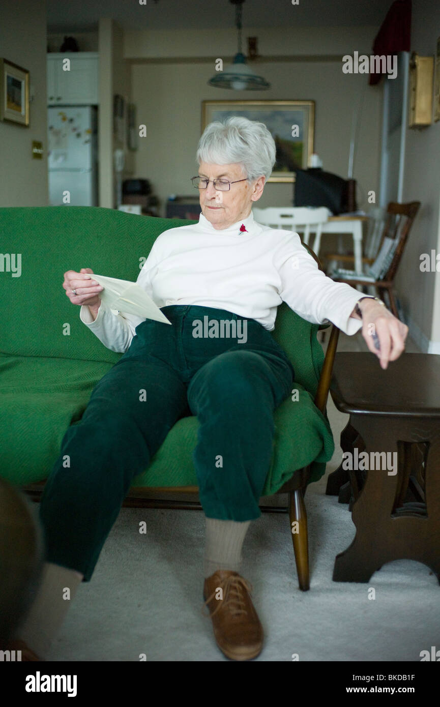 Alte Frau schaut Umschlag auf Couch. Stockfoto