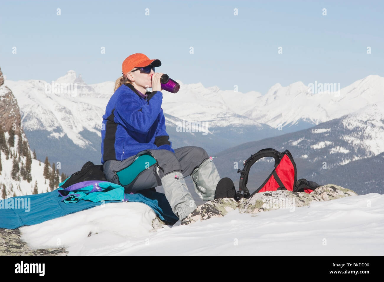 Banff Nationalpark, Alberta, Kanada; Eine weibliche Wanderer setzt zum Rest und nehmen Sie einen Drink und ist umgeben von schneebedeckten Bergen Stockfoto