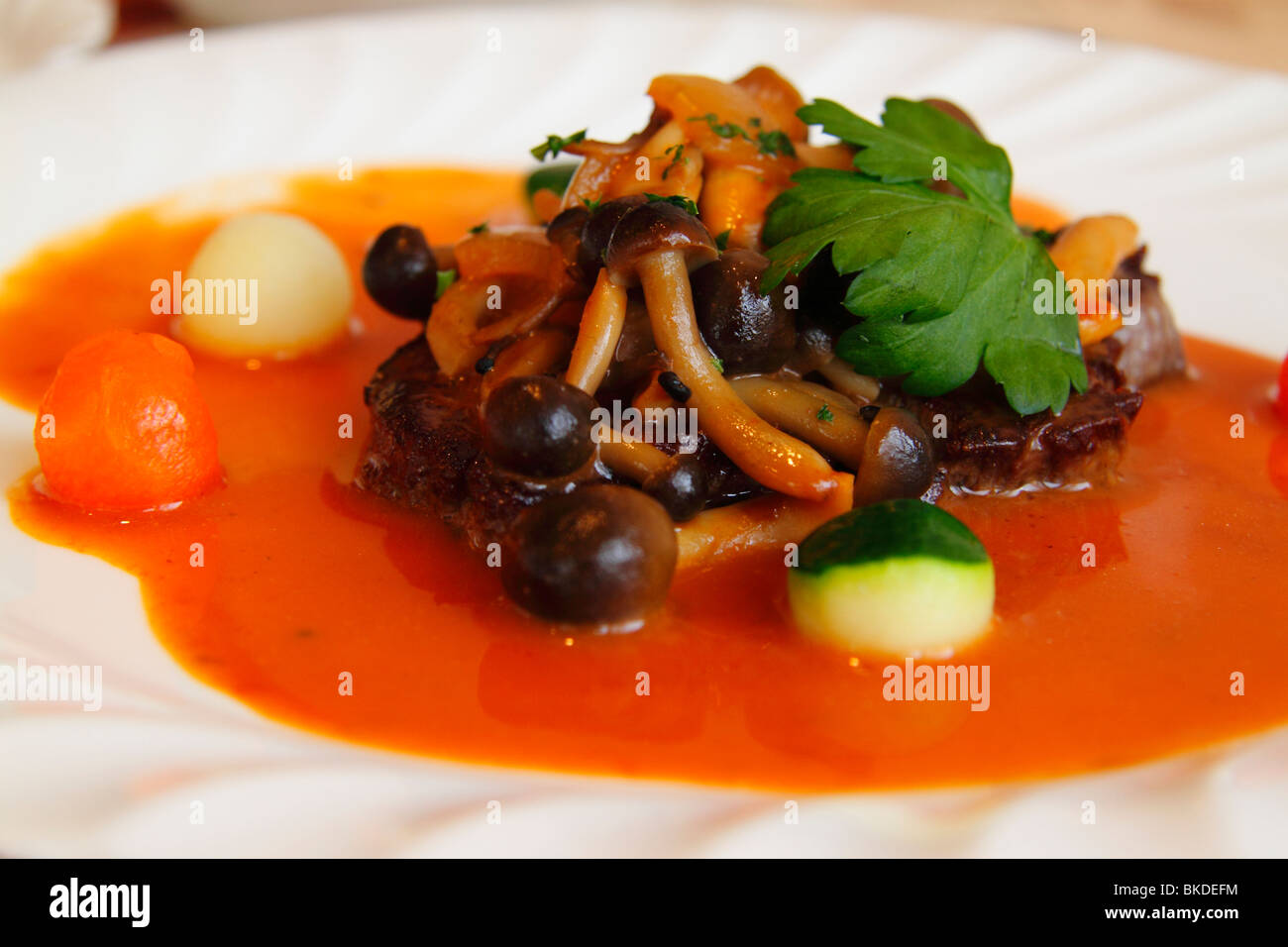 Eine bunte Fleischgericht serviert in einem französischen Bistro von Kyoto dekoriert mit leuchtend orange Soße Sauce, Pilzen und Gemüse. Stockfoto