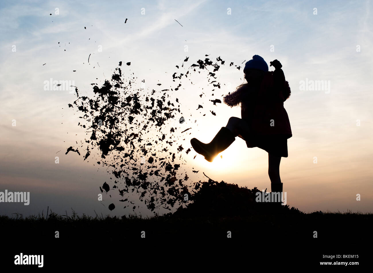Young Girl energetisch Spaß treten einen Stapel Blätter. Silhouette Stockfoto