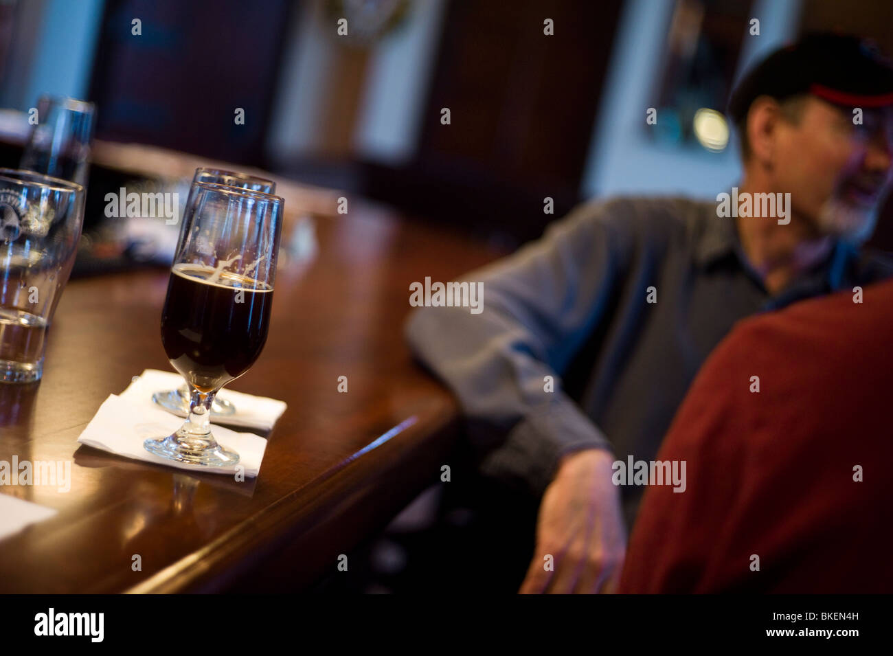 Scharf fokussiert Glas Bier auf Bar mit Mann gelehnt auf Bar. Stockfoto
