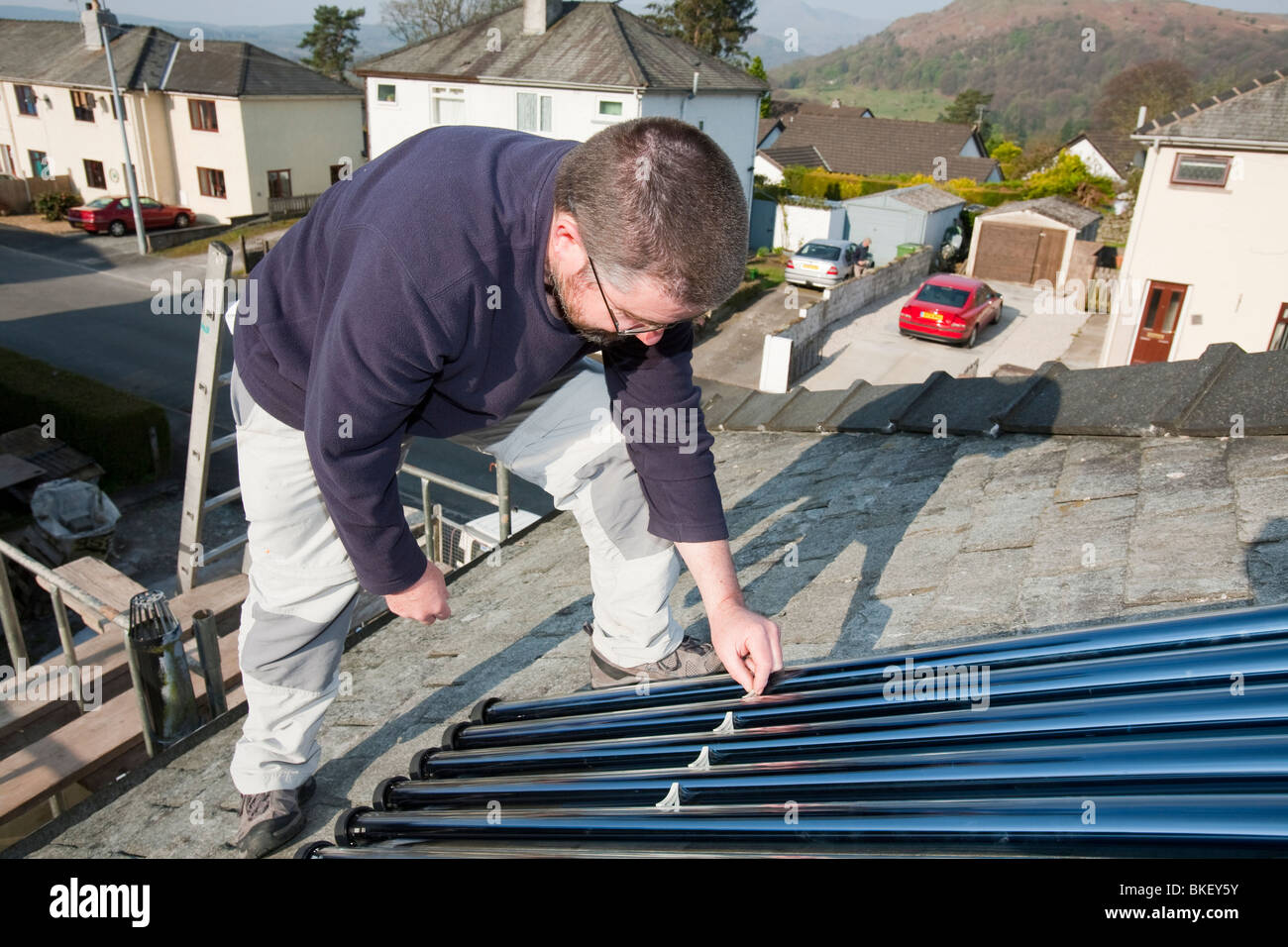 Ein Haushaltsvorstand passend eine solare Warmwasserbereitung Panel auf seinem Hausdach in Ambleside Cumbria UK Stockfoto