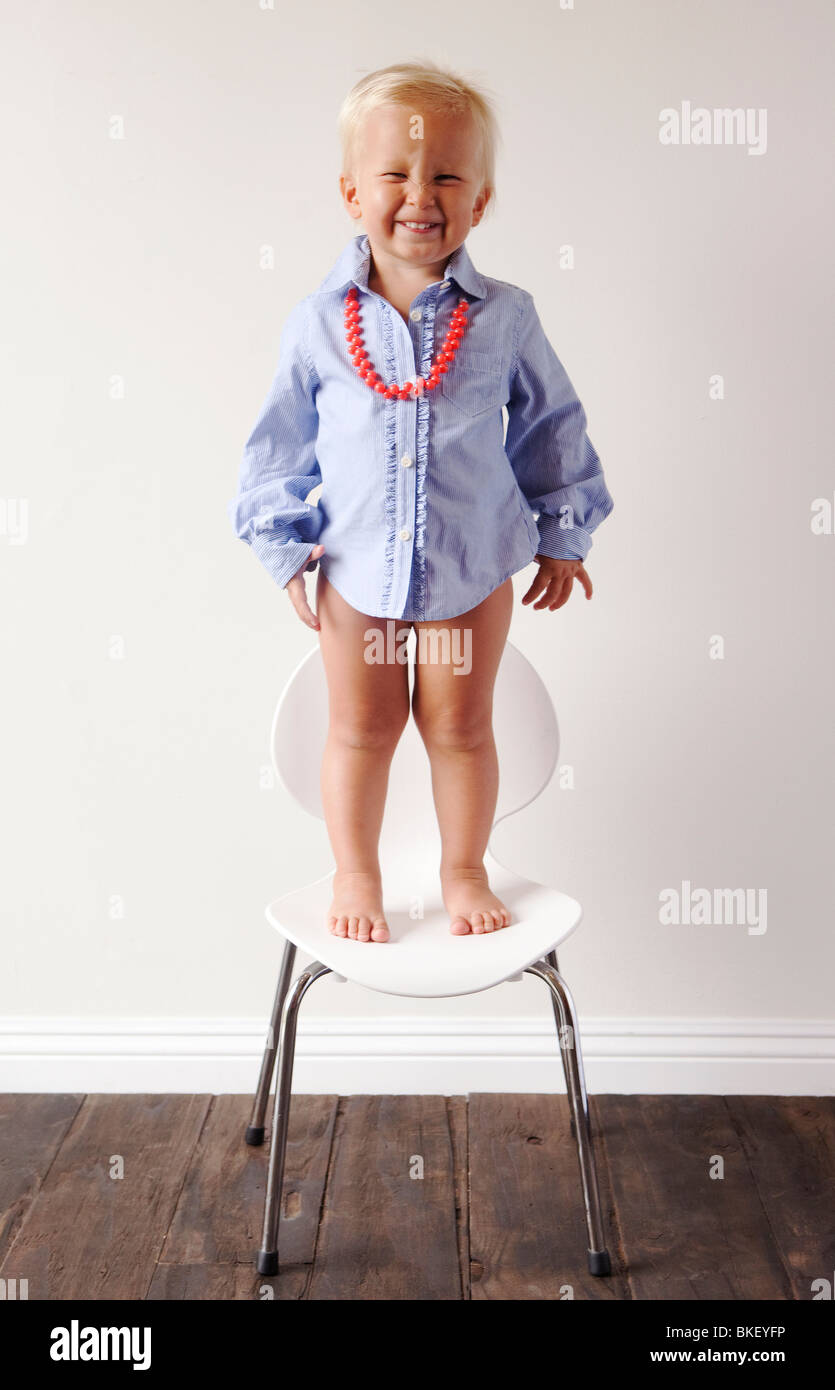 Kleiner Junge im blauen Kleid Shirt stehen auf Stuhl Stockfoto