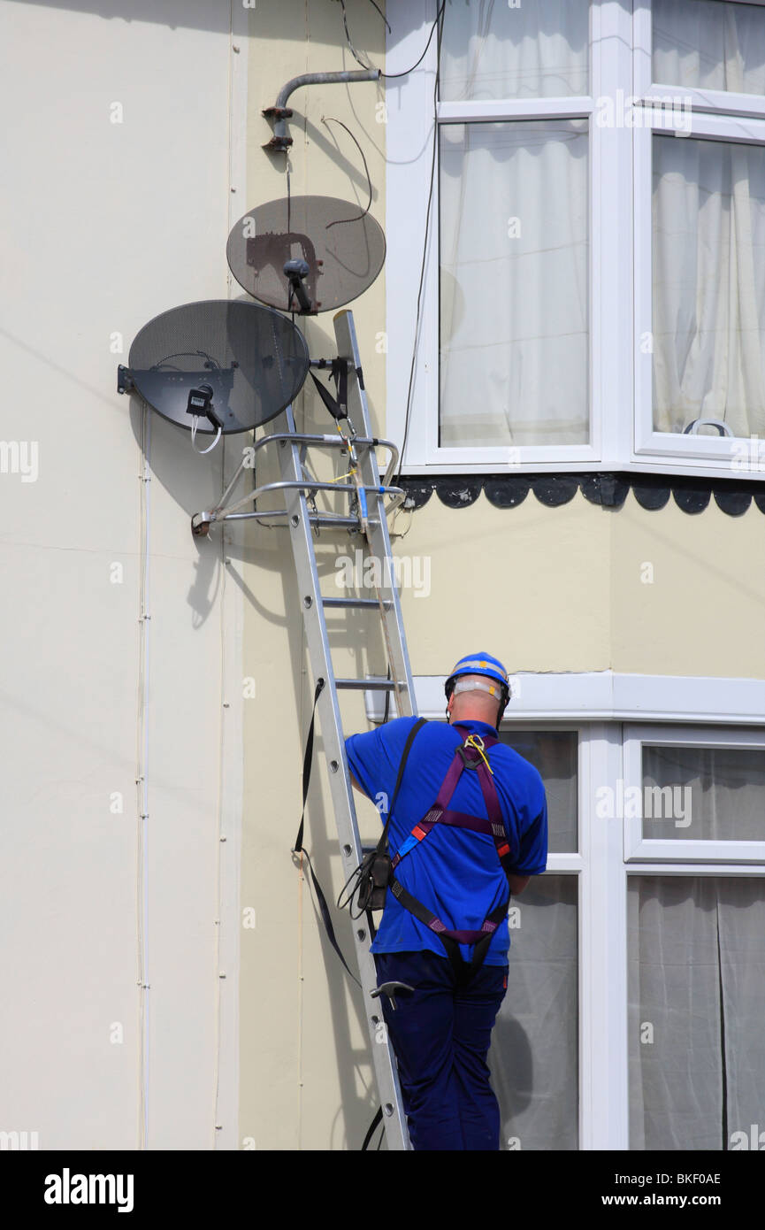 Ein Ingenieur, der Installation einer Satellitenschüssel zu einem Haus in einer Stadt, U.K. Stockfoto