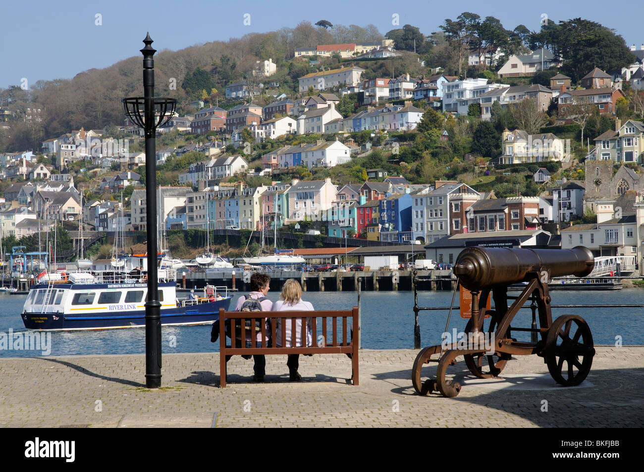 Zwei Frauen sitzen auf einer Holzbank am Flussufer bei Dartmouth mit Blick auf den Fluss Dart & Kingswear South Devon England UK Stockfoto