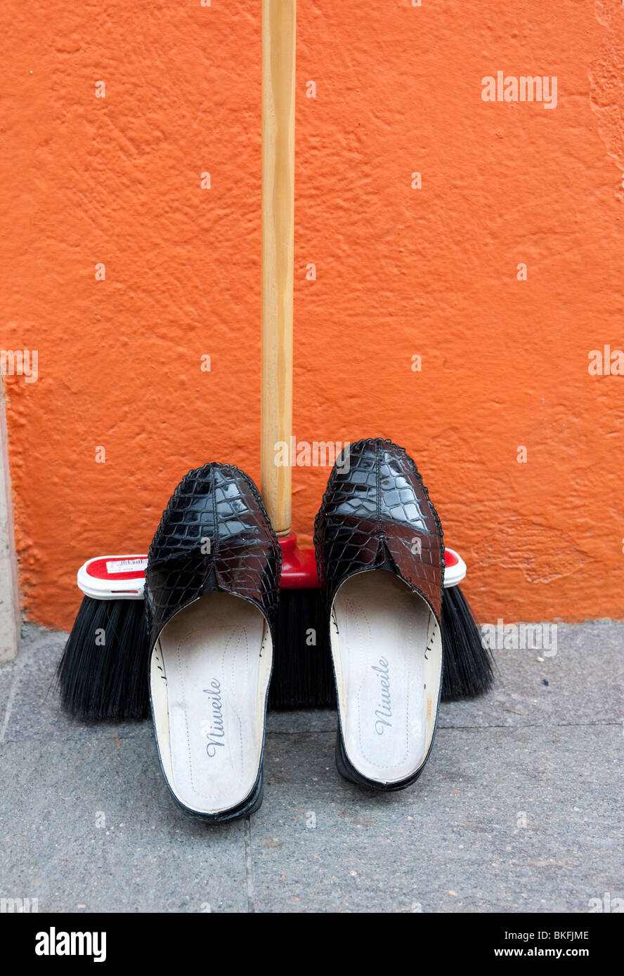 Detail der Schuhe ruht auf Besen vor bunten orange Haus in Burano in der Nähe von Venedig Italien Stockfoto