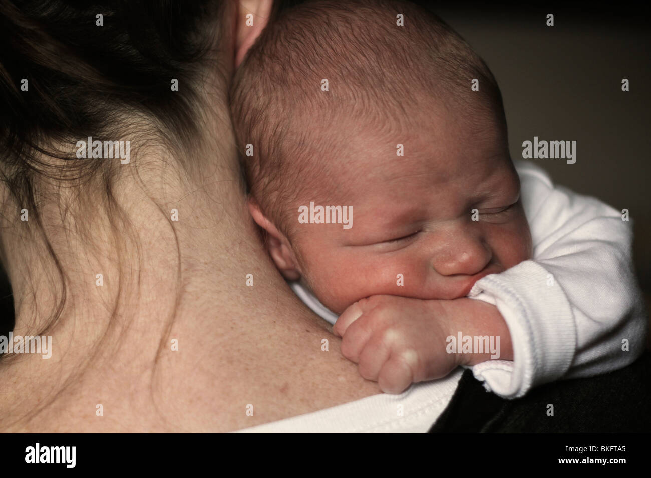 Über die Schulter-Foto von einer Mutter hält liebevoll ein neugeborenes Baby Boy. Das Baby sieht getröstet und Mutter umarmt Stockfoto