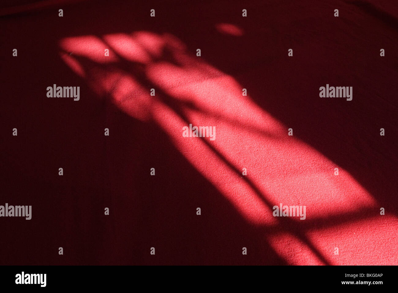 Innen Schlafzimmer Detail. Muster von Licht durch Fenster Vorhang auf rote Bettdecke. Stockfoto