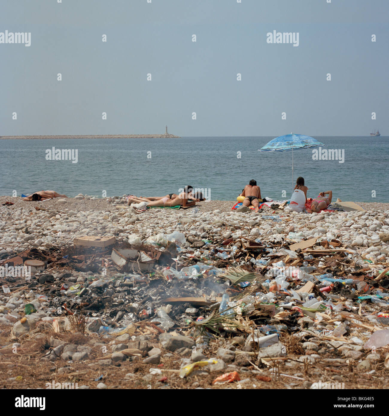 Urlauber, die Sonnenbaden auf einem Kieselstrand mit Müll verbrennen im Vordergrund Stockfoto