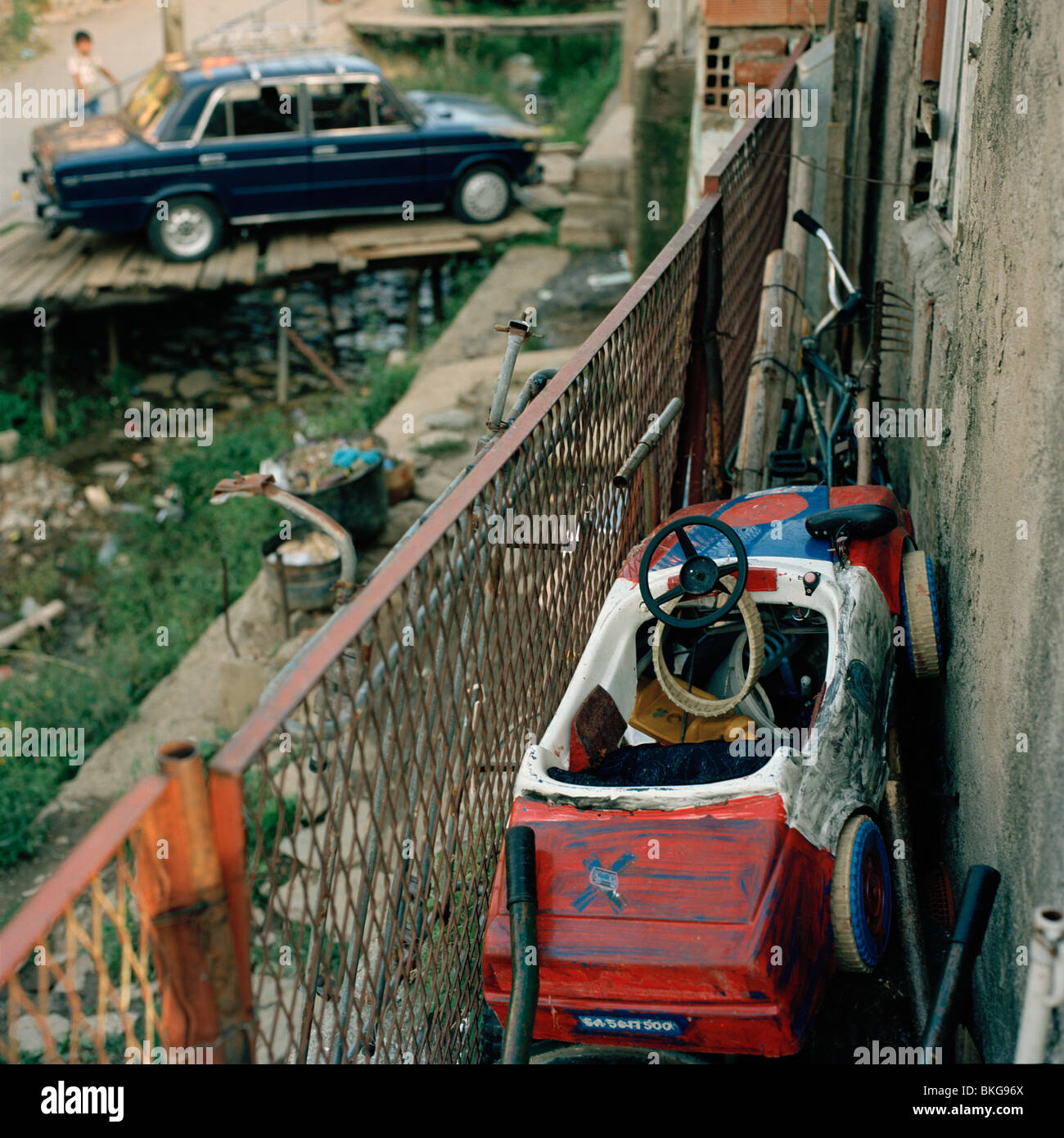 gut gebrauchte Spielzeugauto auf Balkon des baufälligen Haus gespeichert und ein blaues echten altmodisches Trabant Auto geparkt im Hintergrund Stockfoto