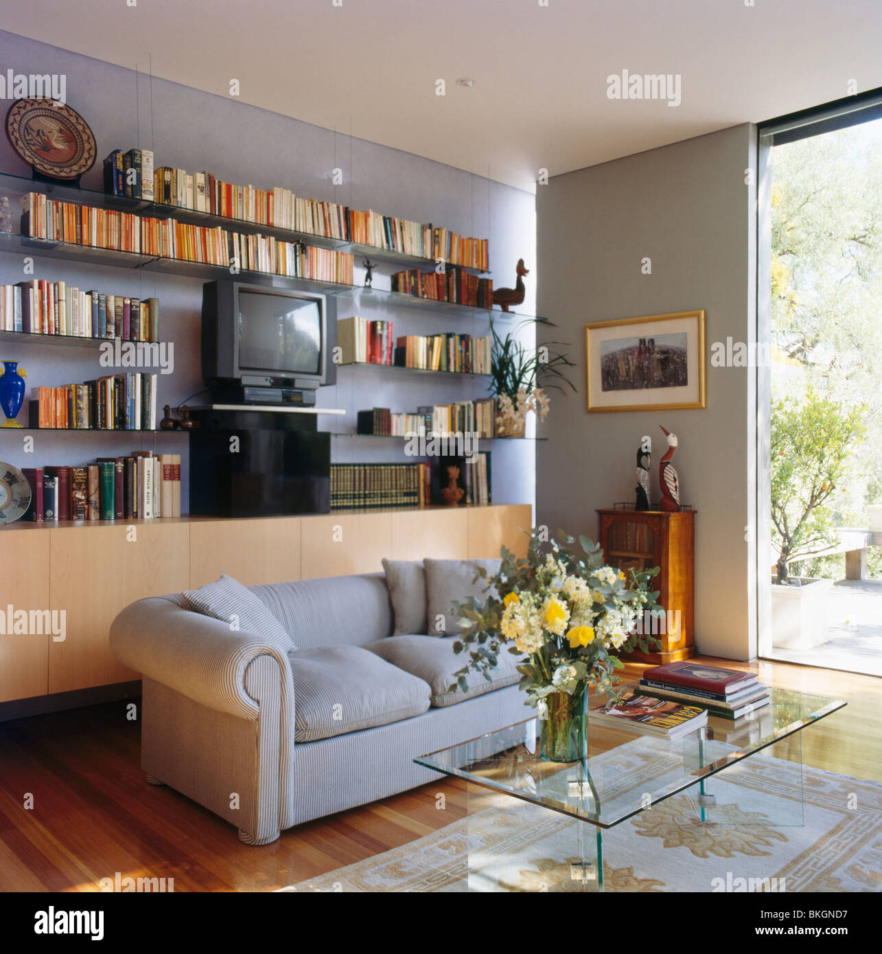 Bücherregale an Wand hinter grauen Sofa in kleinen modernen grauen  Wohnzimmer mit Couchtisch aus Glas Stockfotografie - Alamy