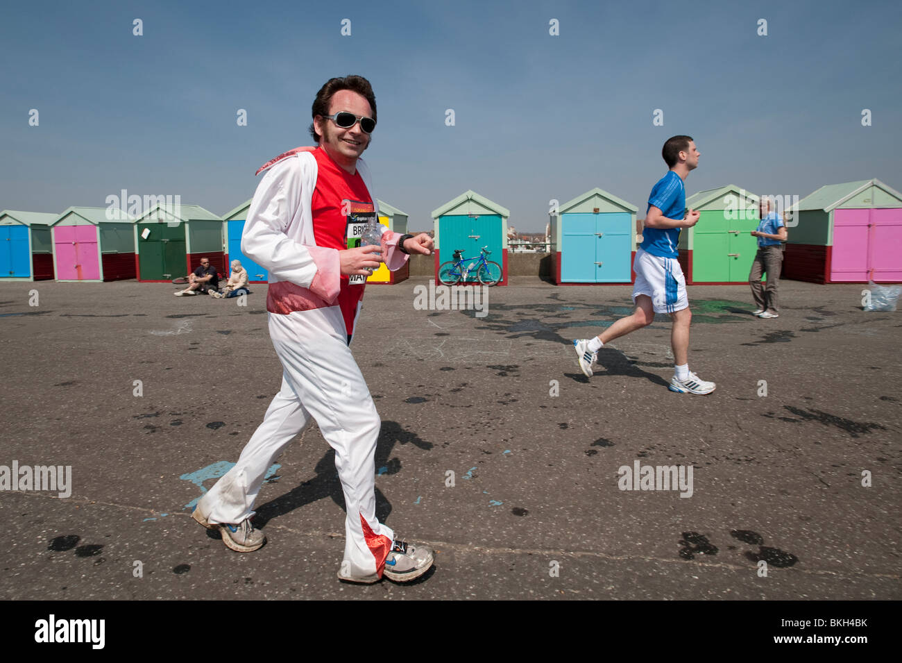 Ein Läufer gekleidet wie ELVIS vorbei Strandhütten auf der Promenade in Hove in den letzten paar Meilen von Brighton Marathon läuft Stockfoto Ein Läufer gekleidet wie ELVIS vorbei Strandhütten auf der Promenade in Hove in den letzten paar Meilen von Brighton Marathon läuft Stockfoto